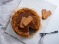 Pyszny sernik Lotus z polewą karmelową i pokruszonymi ciasteczkami. Obok leżą dwa ciasteczka Lotus i widelec.