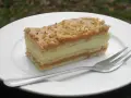Pyszne ciasto krówka bez pieczenia z kremem i orzechami na białym talerzu, obok widelec.