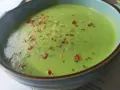 Aksamitna zupa z zielonego groszku, posypana płatkami chili i ziołami, w niebieskiej misce.