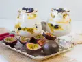 Dwa puchary z Eton Mess, przełożone kremem, marakują i borówkami, ozdobione bezą. Obok owoce marakui i bezy.