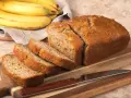 Pyszny, domowy chlebek bananowy, pokrojony na kromki, leży obok dojrzałych bananów.