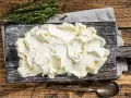 Kremowe mascarpone na desce, obok gałązka tymianku. Czy mascarpone można mrozić? Tak, ale po rozmrożeniu może stracić idealną konsystencję.