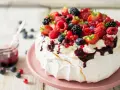 Pyszna beza pavlova obficie udekorowana świeżymi owocami leśnymi i bitą śmietaną, polana musem.