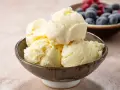 Pyszne, kremowe domowe lody waniliowe w miseczce, obok miseczka z jagodami i malinami.