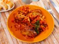 Pyszne żeberka w kapuście, duszona z warzywami, podane na pomarańczowym talerzu. Obok kromki chleba i sztućce.