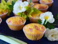 Pyszne muffinki z rabarbarem, ozdobione białymi różami i zielonymi liśćmi, kuszą swoim wyglądem.