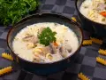 Aksamitna zupa pieczarkowa z makaronem, udekorowana natką pietruszki. Na stole leżą spiralne fusilli, zachęcając do spróbowania.