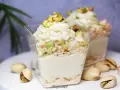 Pyszny deser w pucharku z kremową masą pistacjową, posypany kawałkami pistacji i okruszkami.