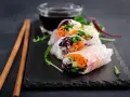 Świeże spring rolls z warzywami i łososiem, podane z sosem.
