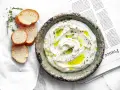 Labneh co to? Kremowy serek jogurtowy, polany oliwą, z ziołami i pieprzem, podany z kromkami bagietki.