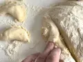 Ręce formują ciasto na pierogi, tworząc półksiężycowate kształty. Mąka rozsypana na blacie.
