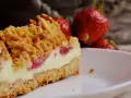 Kruche ciasto z truskawkami, z kremowym nadzieniem i kruszonką, na talerzyku. Obok leżą świeże truskawki.