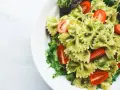 Pyszny makaron z pesto, udekorowany pomidorkami koktajlowymi i świeżą sałatą, podany na białym talerzu.