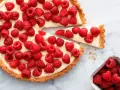 Pyszna tarta z malinami, udekorowana świeżymi owocami, kusi apetycznym wyglądem.