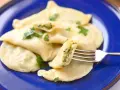 Pyszne pierogi ze szpinakiem i serem, udekorowane natką pietruszki, czekają na widelcu.
