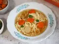 Aksamitny rosół z kaczki z makaronem nitki, marchewką i kawałkami mięsa, ozdobiony natką pietruszki.