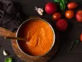 Gęsty, pomidorowy sos w garnku, obok świeże pomidory, czosnek i bazylia. Idealny przepis na to, jak zagęścić sos pomidorowy.