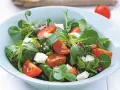 Świeża sałatka z roszponką, pomidorkami koktajlowymi i kostkami sera feta w jasnoniebieskiej misce.