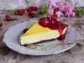 Sernik z polewą z frużeliny wiśniowej i świeżymi wiśniami na talerzu, gotowy do degustacji.