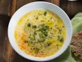 Aromaticzna zupa ogórkowa, pełna koperku i pływających kuleczek tłuszczu, czeka na talerzu obok kromki chleba.