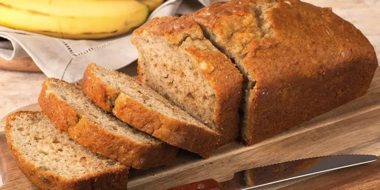Pyszny, domowy chlebek bananowy, pokrojony na kromki, leży obok dojrzałych bananów.