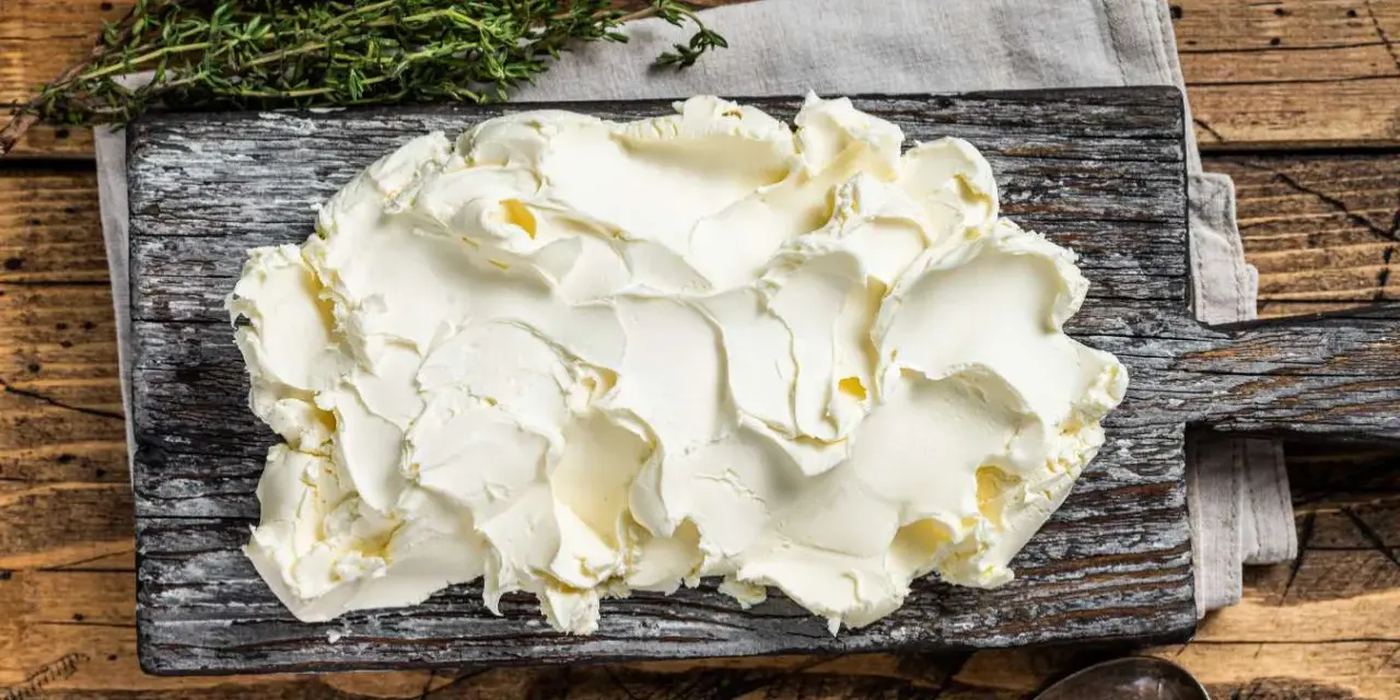 Kremowe mascarpone na desce, obok gałązka tymianku. Czy mascarpone można mrozić? Tak, ale po rozmrożeniu może stracić idealną konsystencję.
