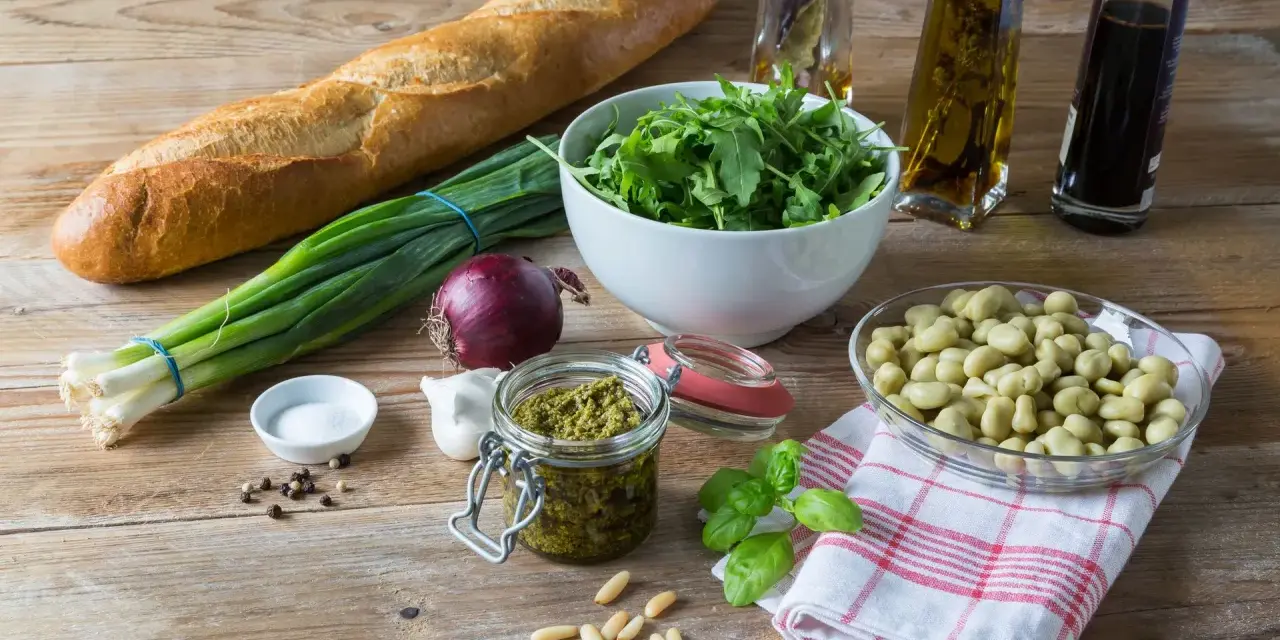 Składniki na pyszne pesto z bobu: świeży bób, bazylia, orzeszki piniowe, czosnek, oliwa, bagietka i rukola.