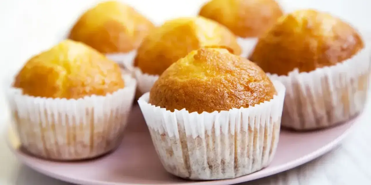 Idealny przepis na wilgotne i puszyste muffinki. Złociste, pachnące babeczki na różowym talerzyku.