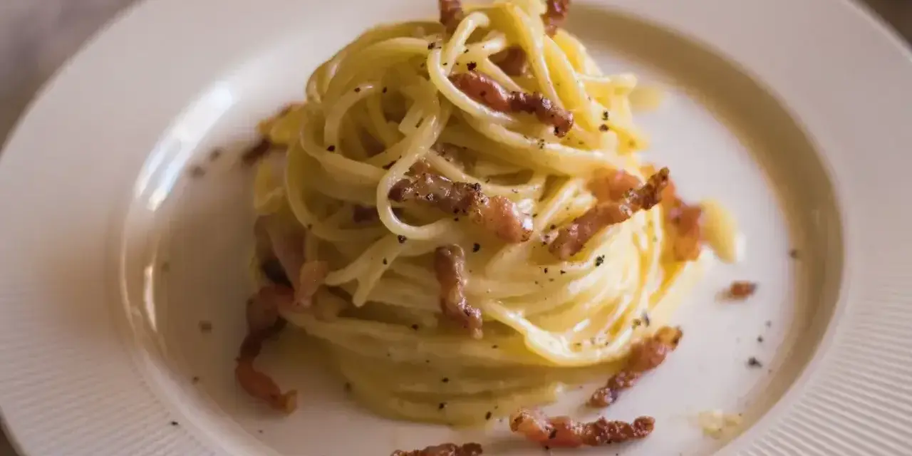 Pyszna carbonara bez śmietany, z chrupiącym boczkiem i czarnym pieprzem, podana na białym talerzu.
