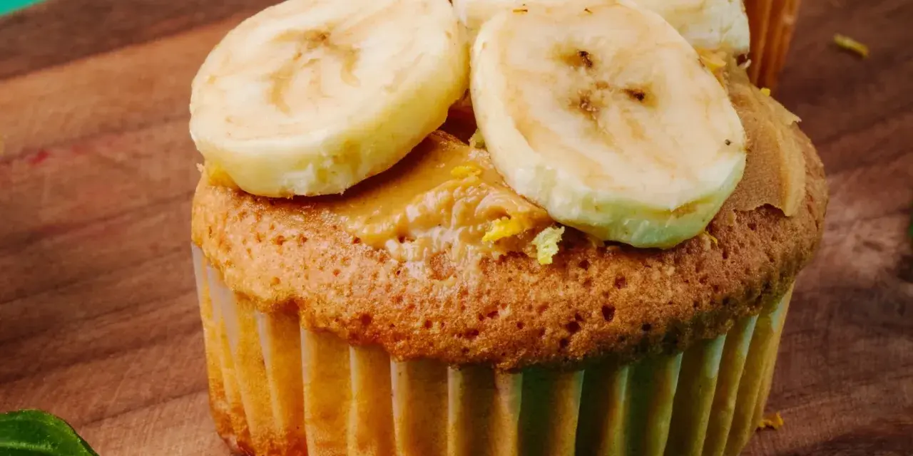 Pyszne muffinki bananowe z kremem orzechowym i plasterkami banana na drewnianej desce.