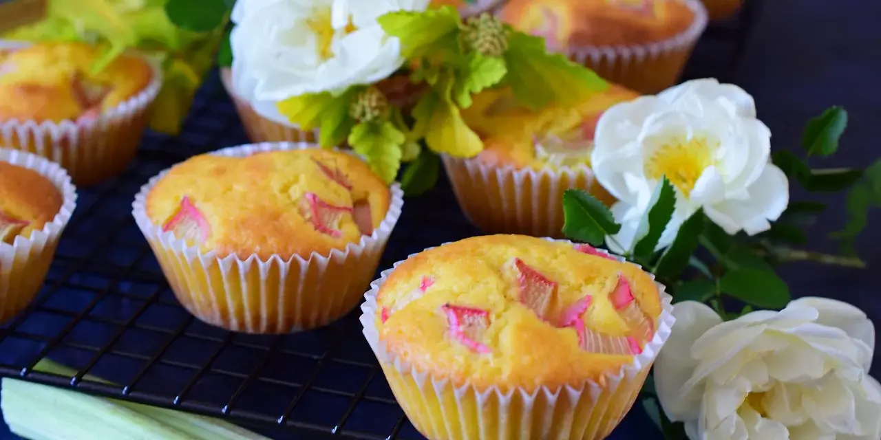 Pyszne muffinki z rabarbarem, ozdobione białymi różami i zielonymi liśćmi, kuszą swoim wyglądem.