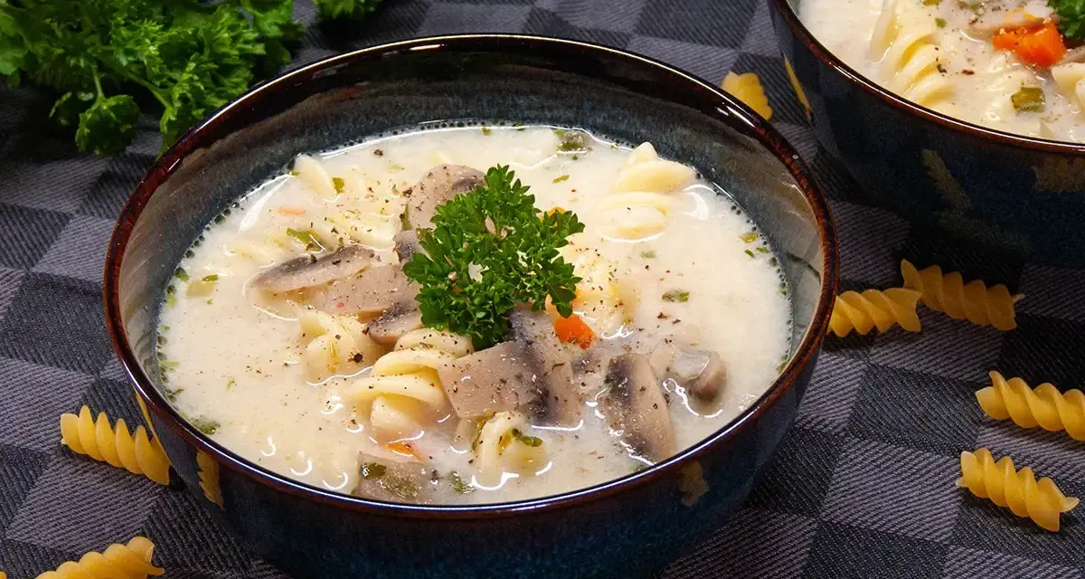 Aksamitna zupa pieczarkowa z makaronem, udekorowana natką pietruszki. Na stole leżą spiralne fusilli, zachęcając do spróbowania.