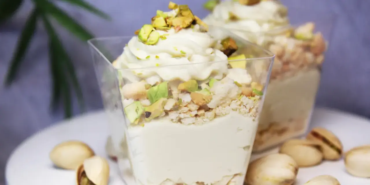 Pyszny deser w pucharku z kremową masą pistacjową, posypany kawałkami pistacji i okruszkami.