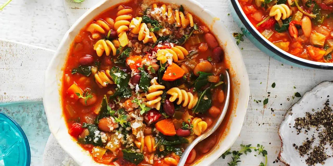 Minestrone co to? Aromatyczna zupa z makaronem, fasolą, warzywami i ziołami, podana w białej misce.