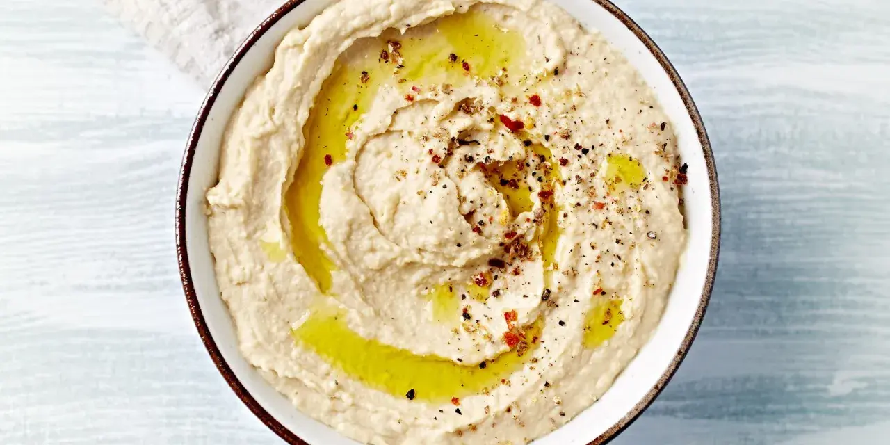 Kremowy hummus polany oliwą, posypany pieprzem i papryką. Idealny do pieczywa, jako dodatek do dań. Prosty hummus przepis.