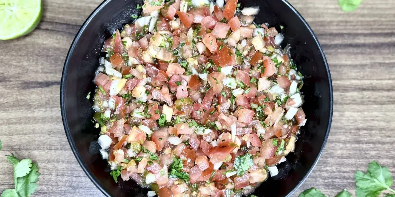 Świeże, posiekane pomidory, cebula, kolendra i papryczka jalapeno tworzą apetyczne pico de gallo w czarnej misce.