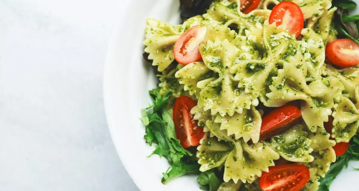 Pyszny makaron z pesto, udekorowany pomidorkami koktajlowymi i świeżą sałatą, podany na białym talerzu.