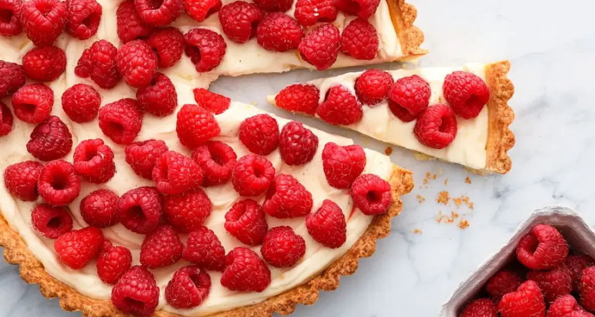 Pyszna tarta z malinami, udekorowana świeżymi owocami, kusi apetycznym wyglądem.