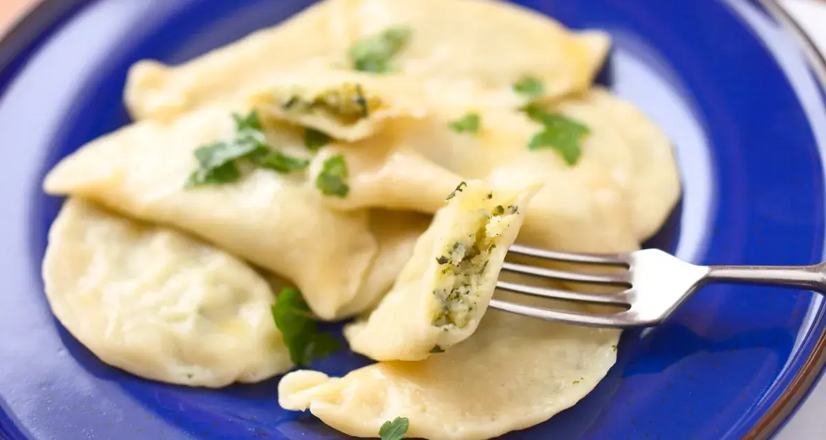 Pyszne pierogi ze szpinakiem i serem, udekorowane natką pietruszki, czekają na widelcu.