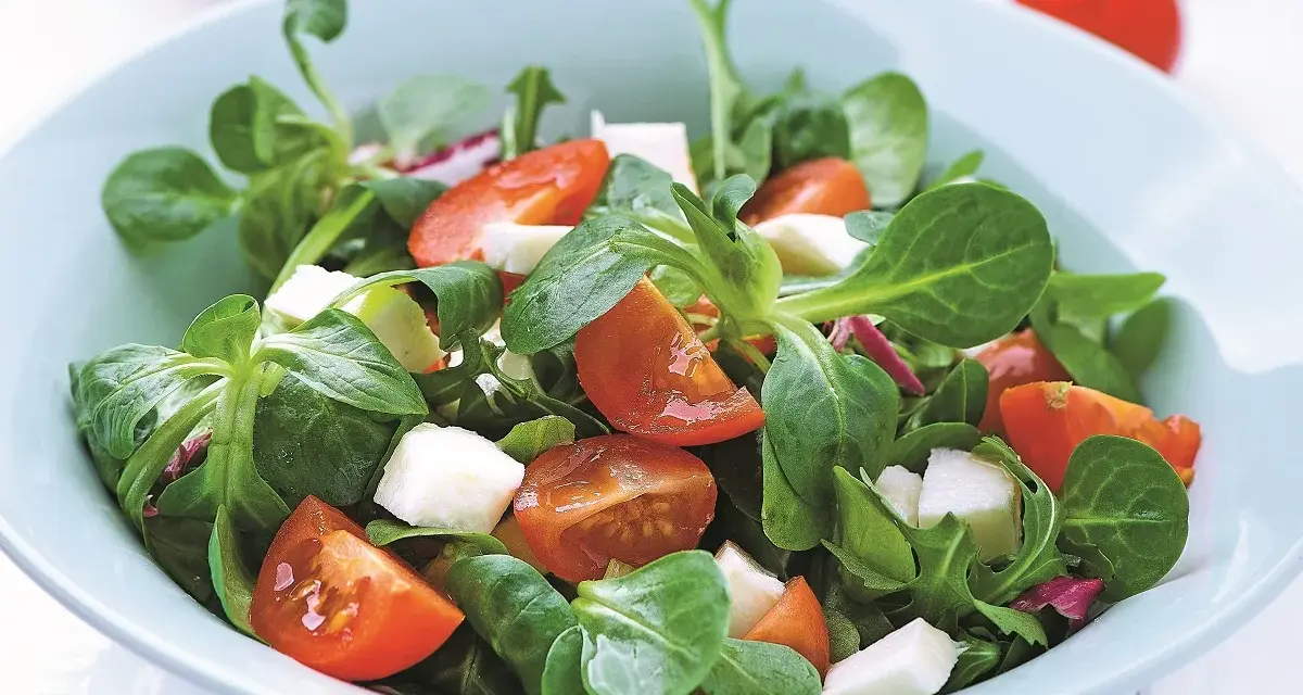 Świeża sałatka z roszponką, pomidorkami koktajlowymi i kostkami sera feta w jasnoniebieskiej misce.