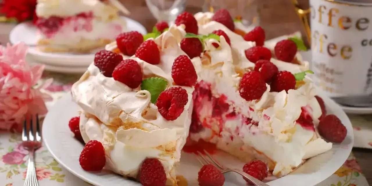 Pyszny tort bezowy z malinami, udekorowany listkami mięty. Idealny deser na letnie popołudnie.
