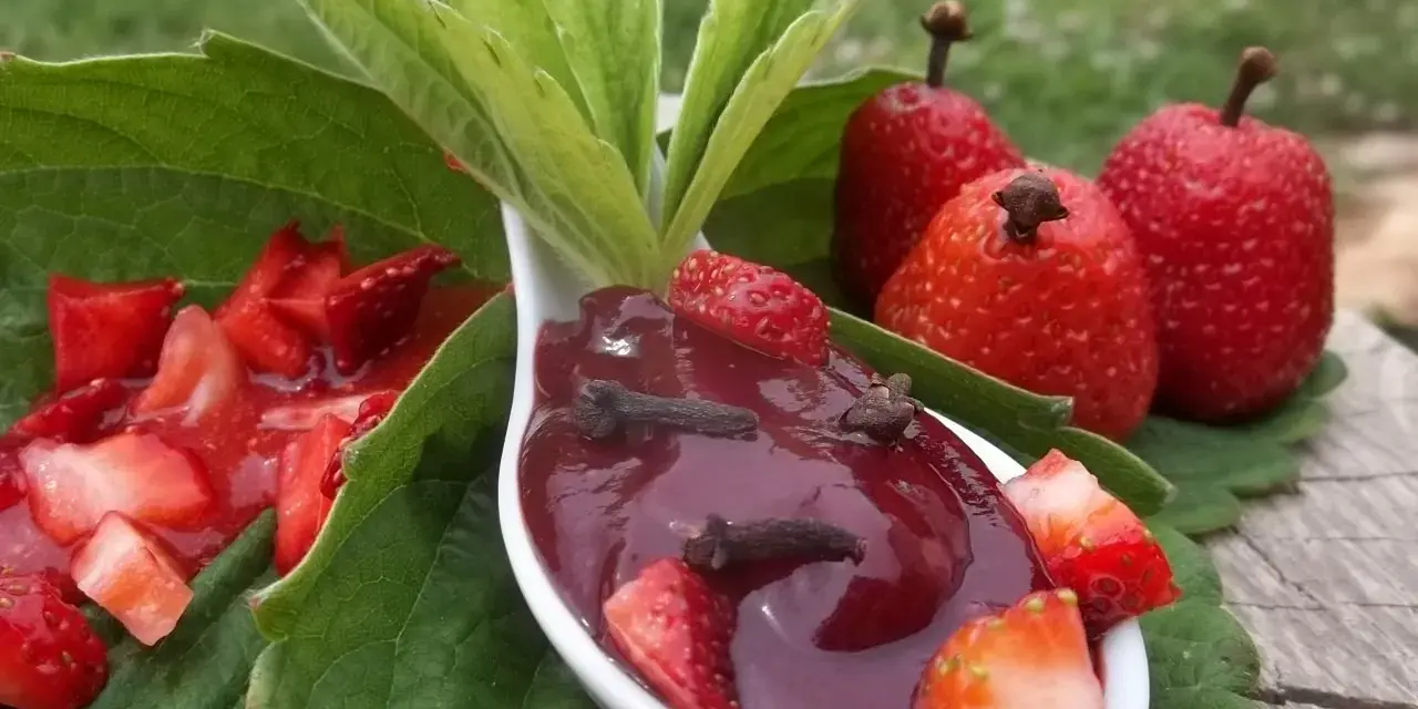 Aksamitna konfitura z truskawek z goździkami na łyżce, otoczona świeżymi owocami i liśćmi.
