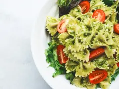Pyszny makaron z pesto, udekorowany pomidorkami koktajlowymi i świeżą sałatą, podany na białym talerzu.