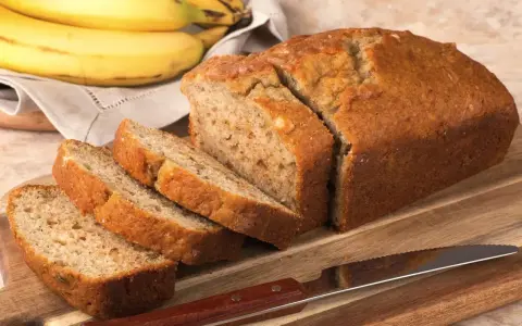 Pyszny, domowy chlebek bananowy, pokrojony na kromki, leży obok dojrzałych bananów.
