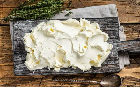 Kremowe mascarpone na desce, obok gałązka tymianku. Czy mascarpone można mrozić? Tak, ale po rozmrożeniu może stracić idealną konsystencję.