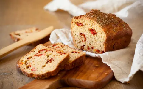 A pyszny chleb z suszonymi pomidorami, pokrojony na kromki, leży na drewnianej desce.
