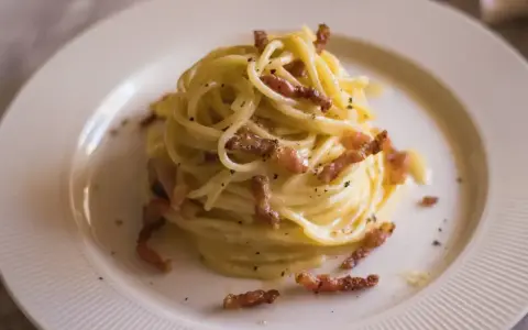 Pyszna carbonara bez śmietany, z chrupiącym boczkiem i czarnym pieprzem, podana na białym talerzu.