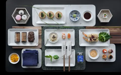 Elegancka aranżacja stołu z różnorodnymi przekąskami, w tym mini naleśnikami z kawiorem, sushi, krewetkami w tempurze i makaronikami. Idealne na wieczór, gdy masz ochotę na coś pysznego do sushi.