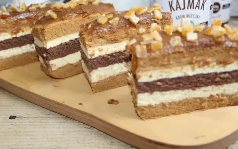Pyszne ciasto z kajmakiem, przełożone kremem i biszkoptem, ozdobione kandyzowanymi skórkami.