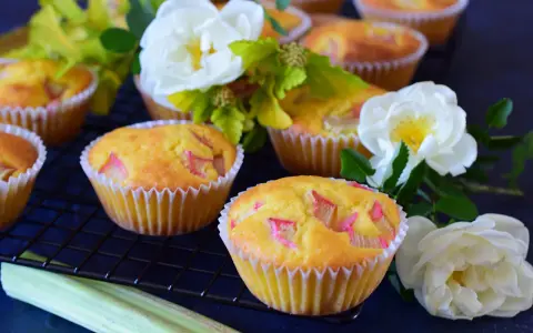 Pyszne muffinki z rabarbarem, ozdobione białymi różami i zielonymi liśćmi, kuszą swoim wyglądem.